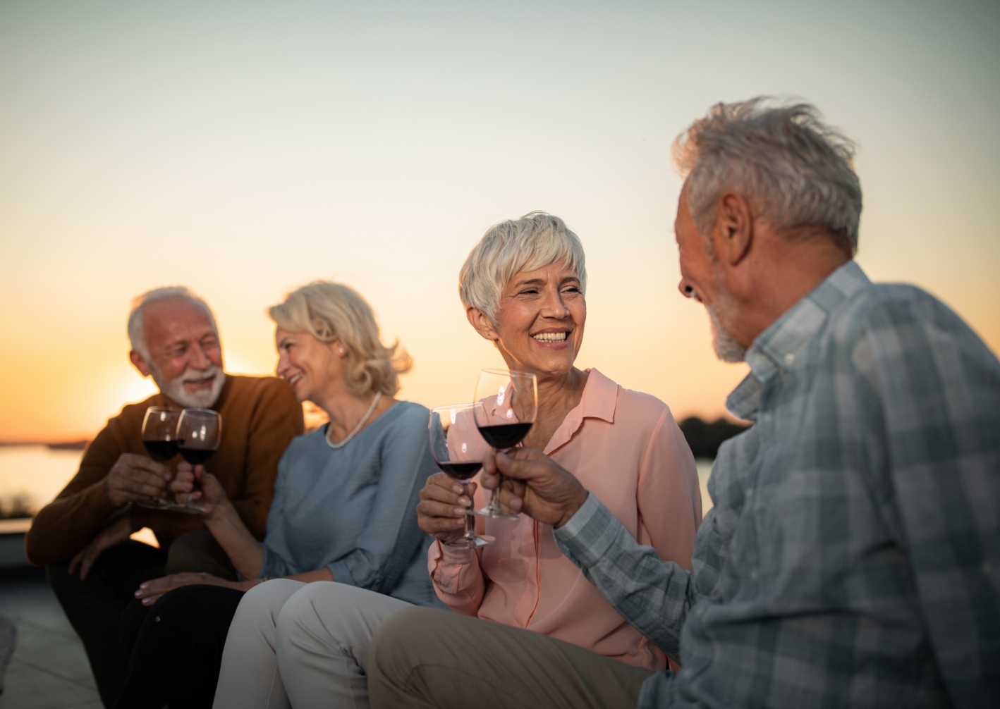 two senior couple friends drinking wine next to a lake at sunset