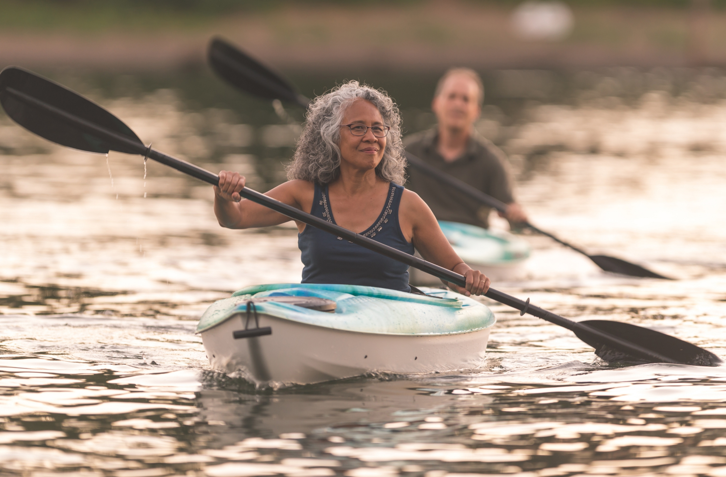 man and woman in separate kayaks paddling on a lake