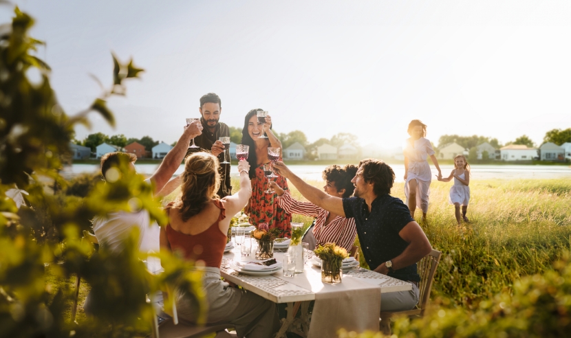 friends and family at a table in the yard raising a glass in cheer as children walk up