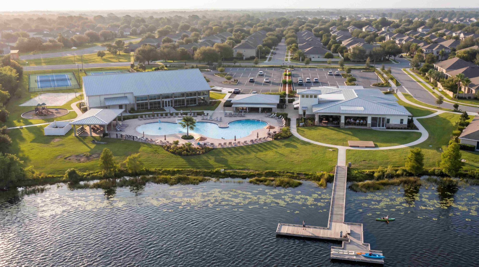 Aerial view of Lakehaven's amenity center featuring a resort-style pool, clubhouse, tennis courts, playground, and private community dock on the lake