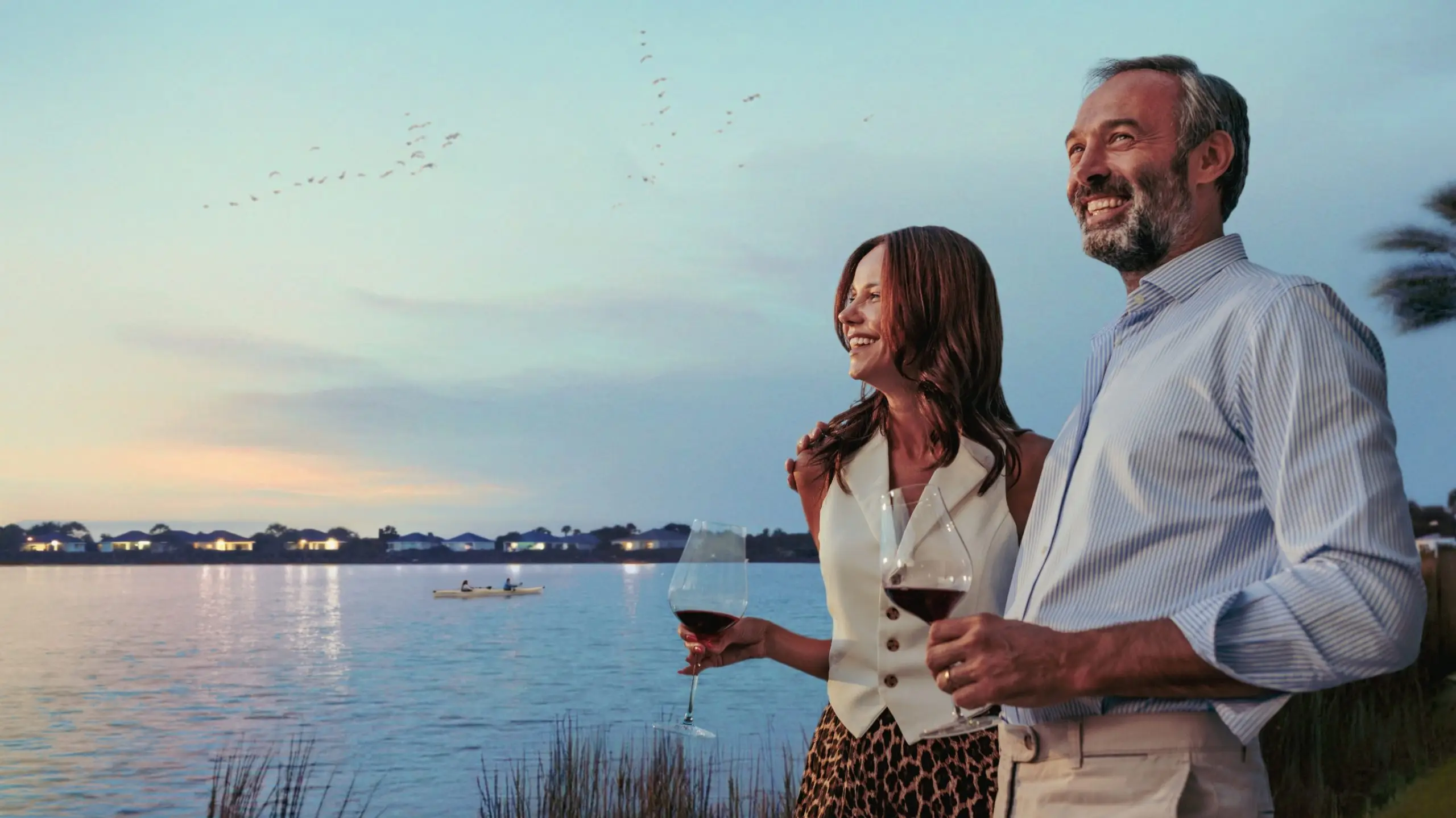Smiling mature couple enjoying a glass of wine by an infinity pool at sunset, looking at the view