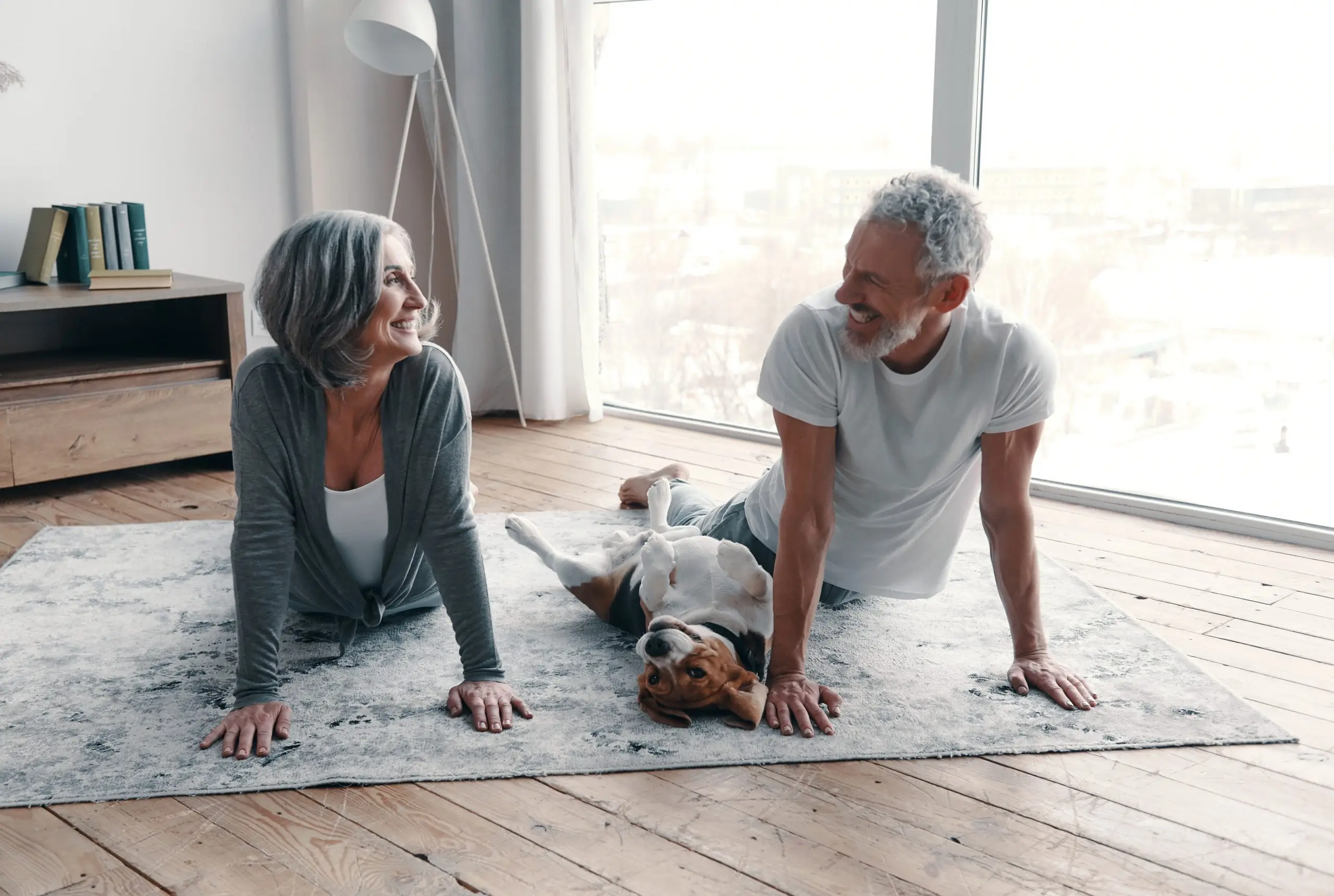 older couple doing yoga in their living room with their dog