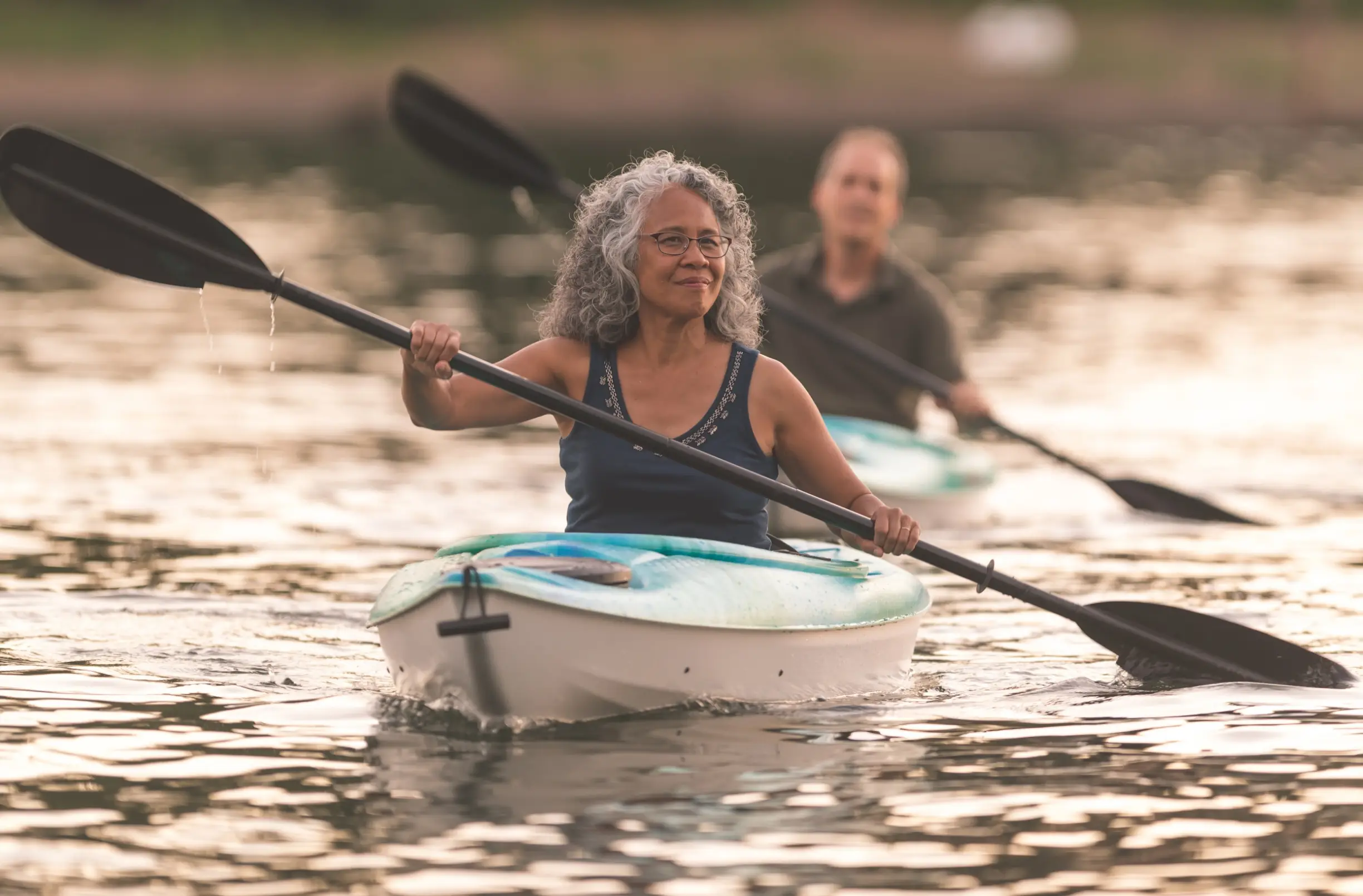 man and woman in separate kayaks paddling on a lake