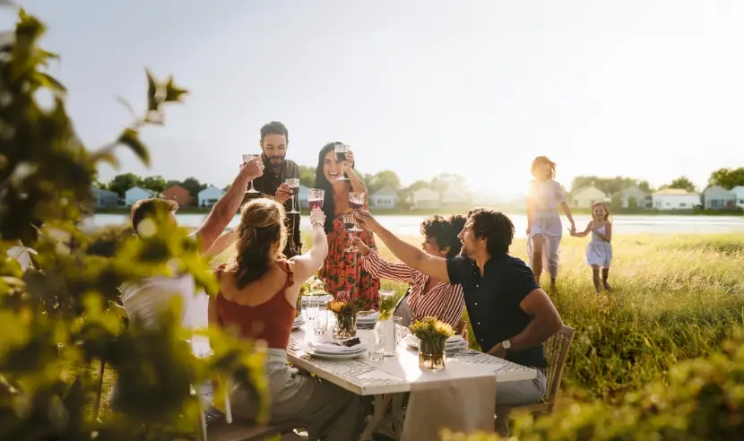 friends and family at a table in the yard raising a glass in cheer as children walk up