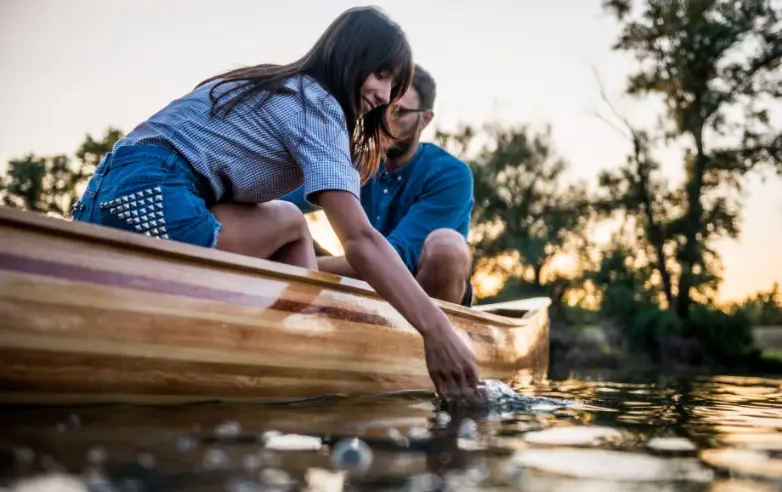 woman and man sitting in a canoe dipping her hand into the water with