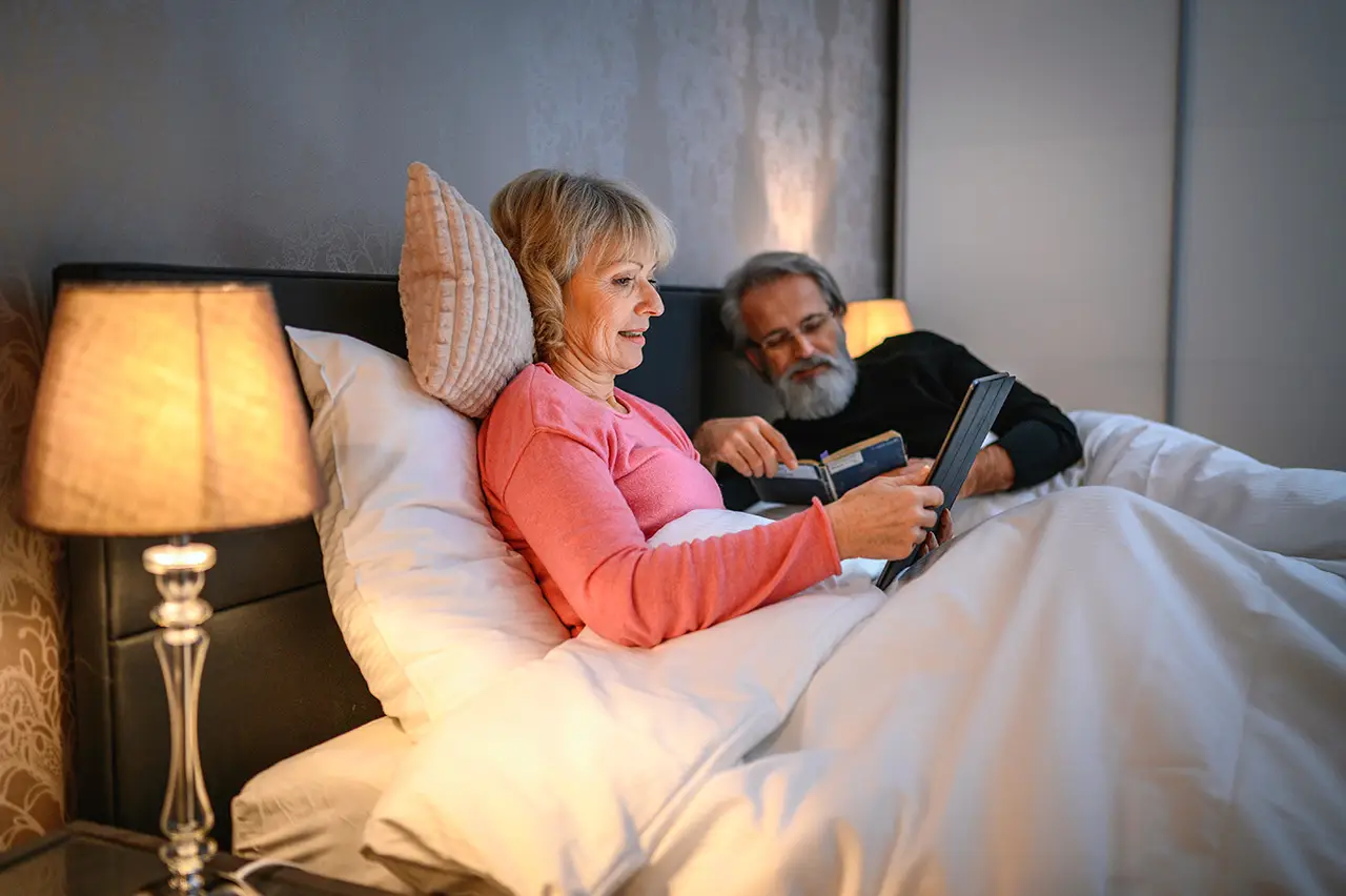 A mature woman reading a book in her bed during the evening