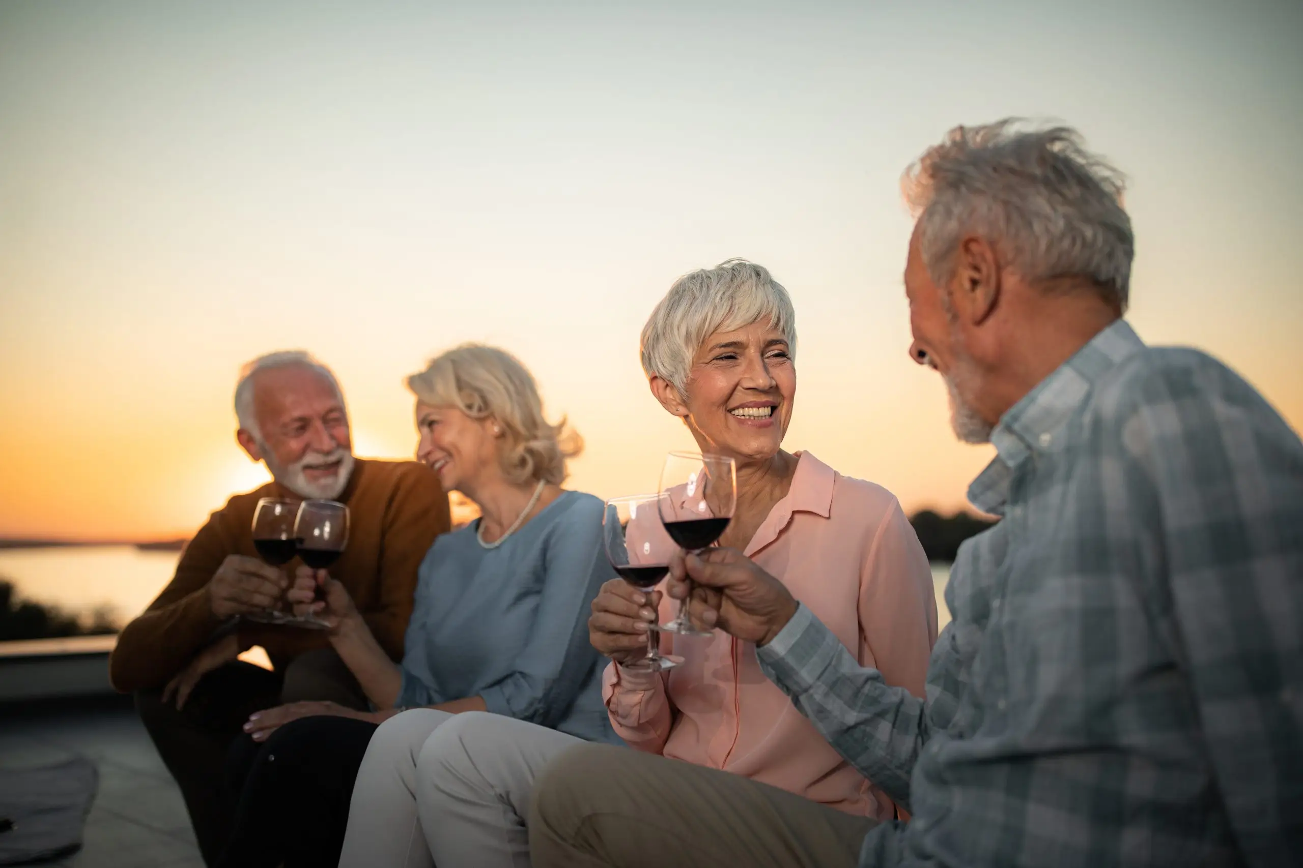 Happy senior couples having fun while toasting among themselves on a roof at sunset. Focus is on woman with short hair. Copy space.
