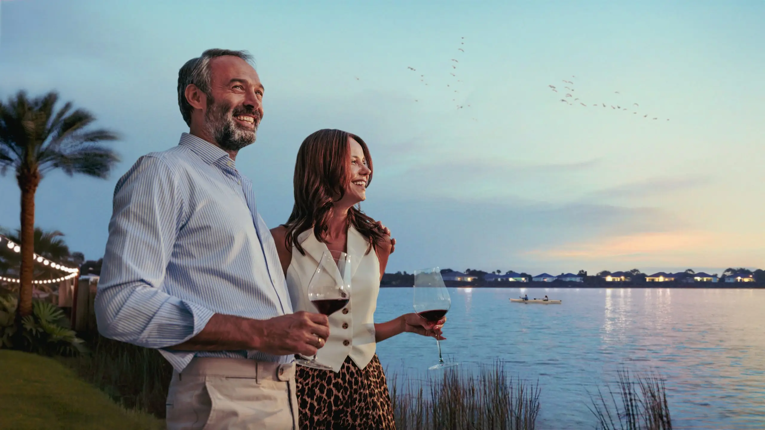 Smiling mature couple enjoying a glass of wine by an infinity pool at sunset, looking at the view