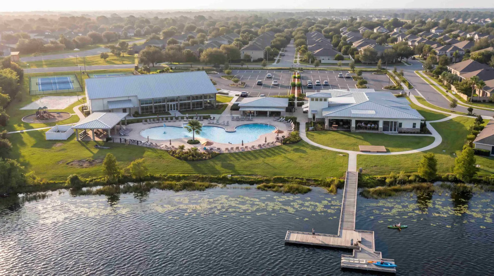 Aerial view of Lakehaven's amenity center featuring a resort-style pool, clubhouse, tennis courts, playground, and private community dock on the lake